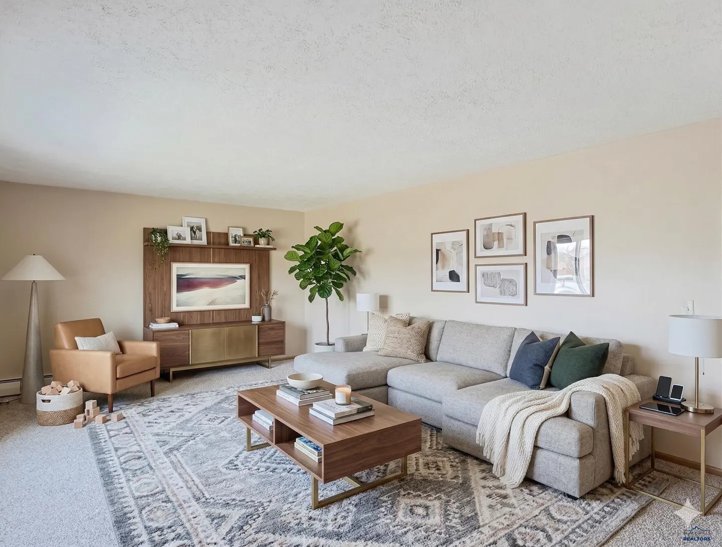 Living room with a gray patterned rug, sectional sofa, wood coffee table, and a TV mounted on a wood and gold media console.