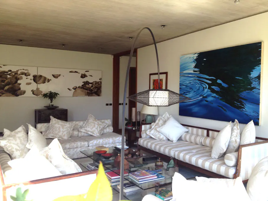 Living room with two sofas, glass coffee table, and artwork. One painting is blue water, the other is rocks. A modern lamp arches over the seating area.