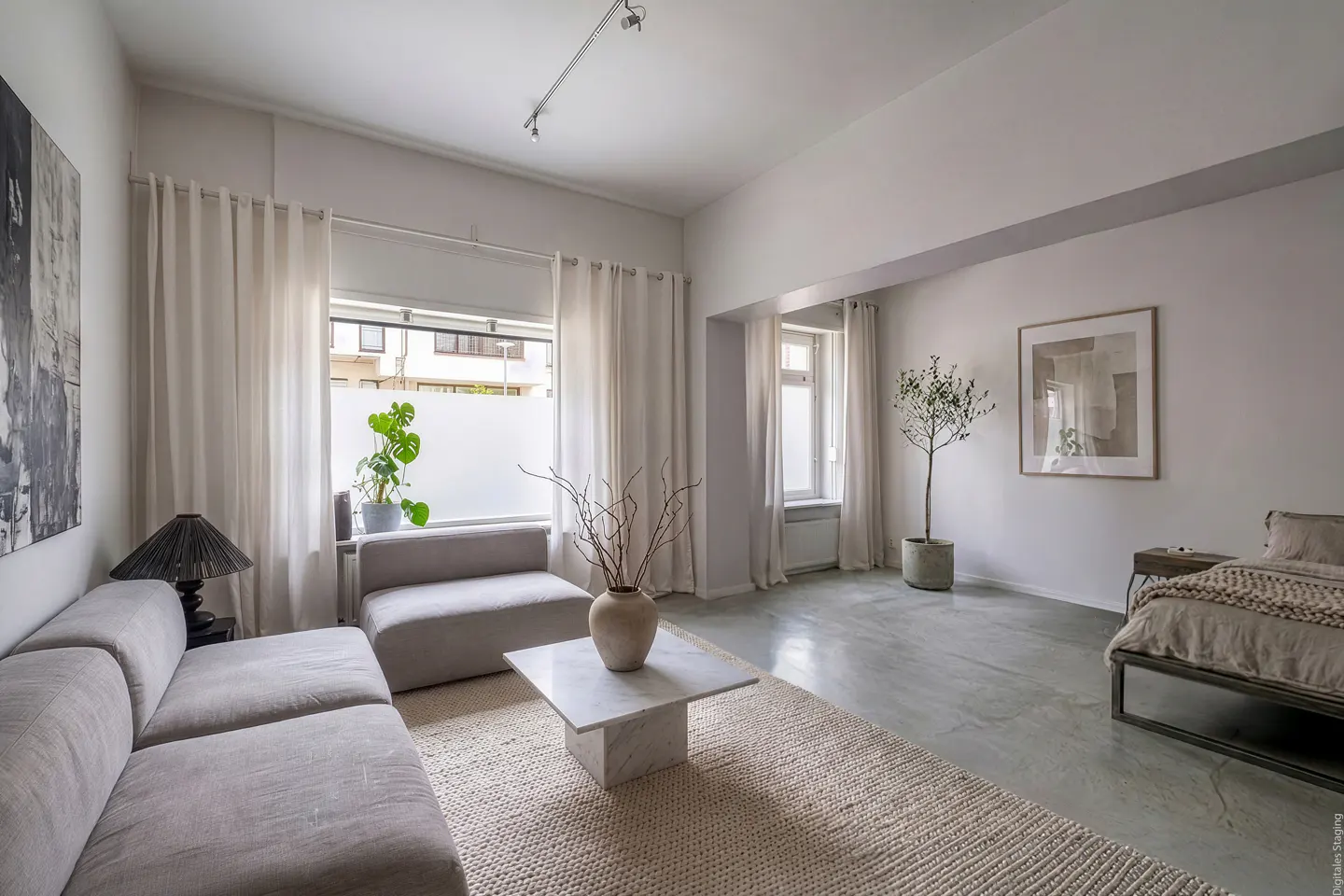 Bright, airy living room with a gray sofa, marble coffee table, and neutral rug. A bed is visible in the background.