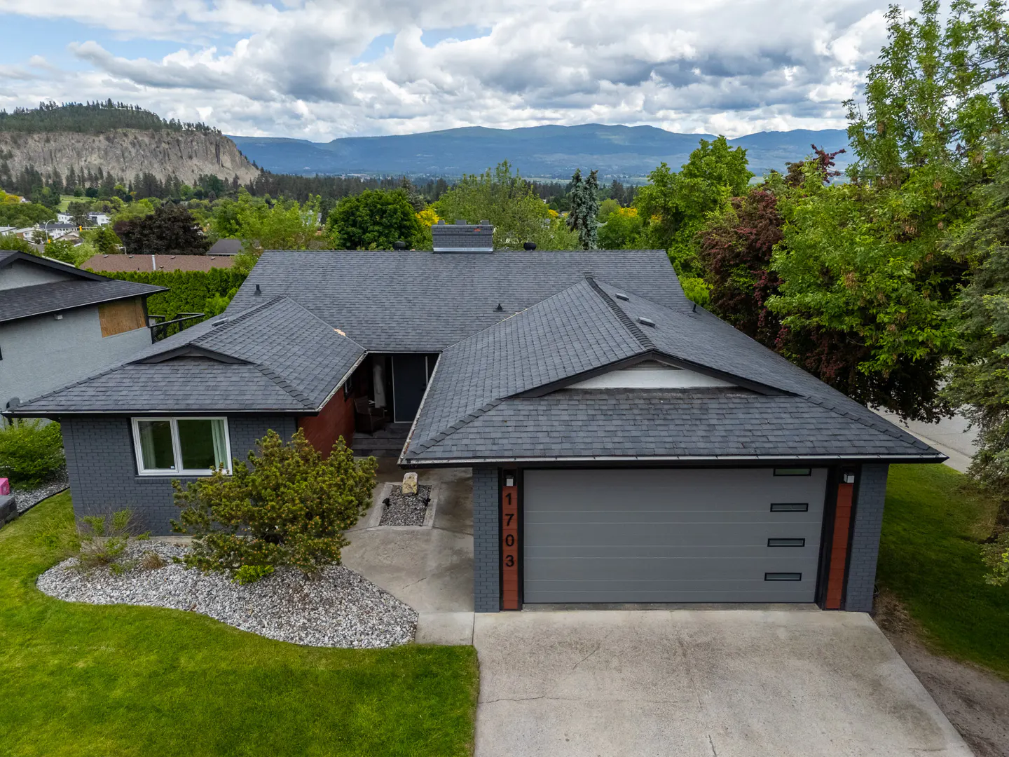 A gray house with a dark roof, green lawn, and a mountain view in the background.