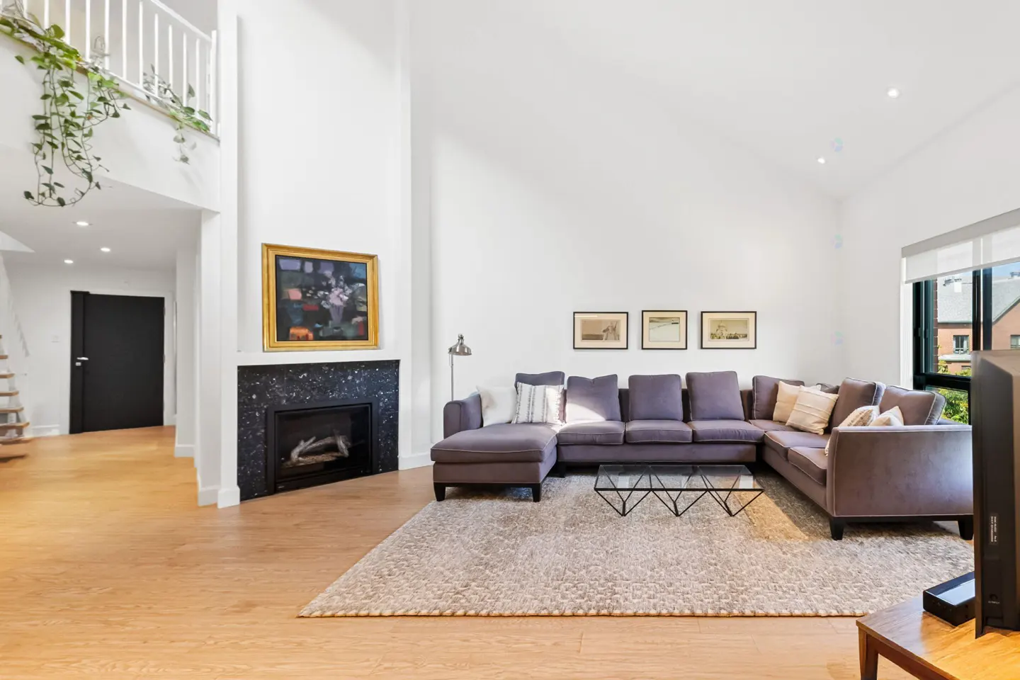 Bright living room with wood floors, a gray sectional sofa, and a black marble fireplace. A painting hangs above the fireplace.
