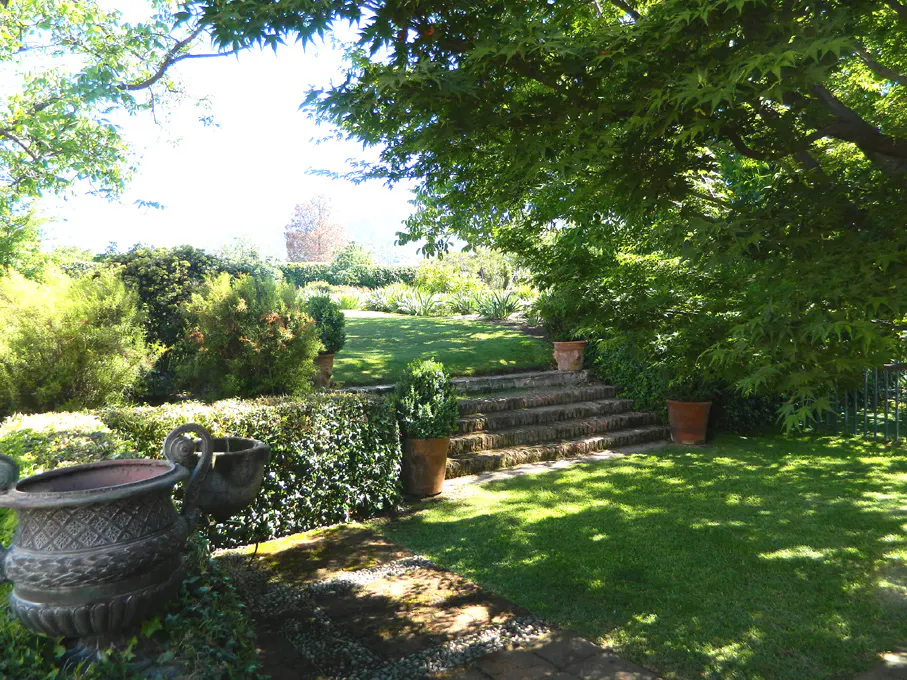 A lush green garden with stone steps leading up a gentle slope, framed by trees and hedges.