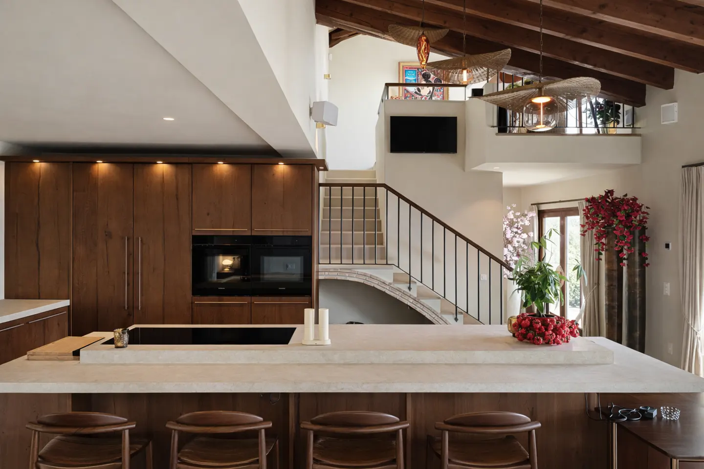 Modern kitchen with wood cabinets, a large stone island with bar stools, and a staircase leading to a lofted area.