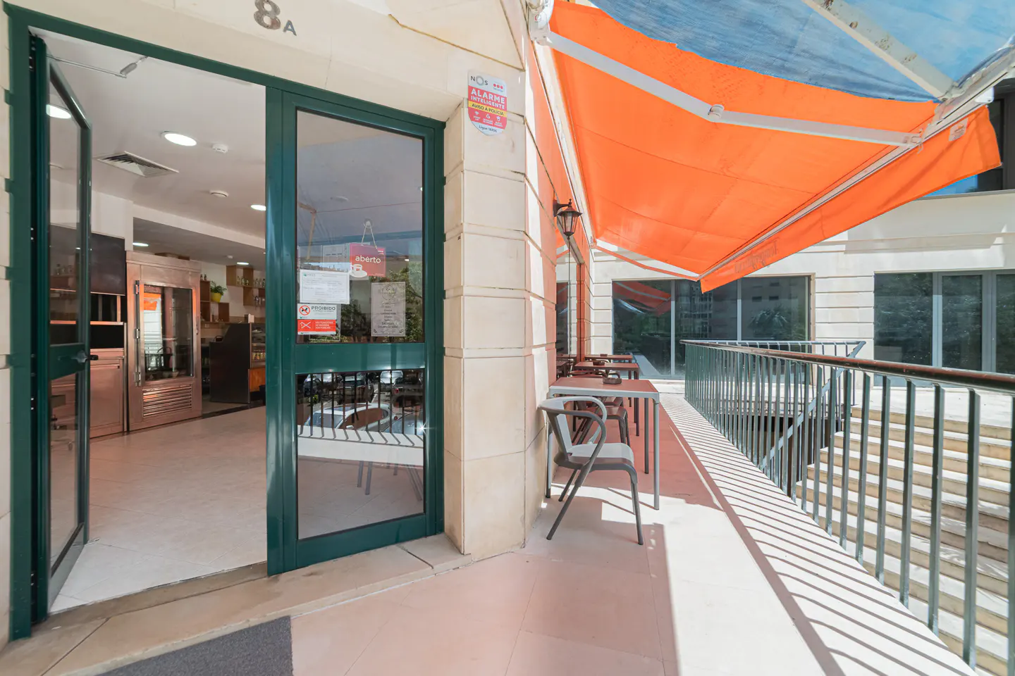 Outdoor cafe with open green door, tables and chairs on patio under orange awning.
