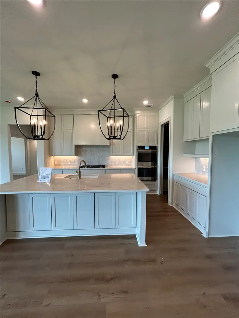 A bright kitchen with white cabinets, a blue island, and wood floors. Black pendant lights hang above the island.