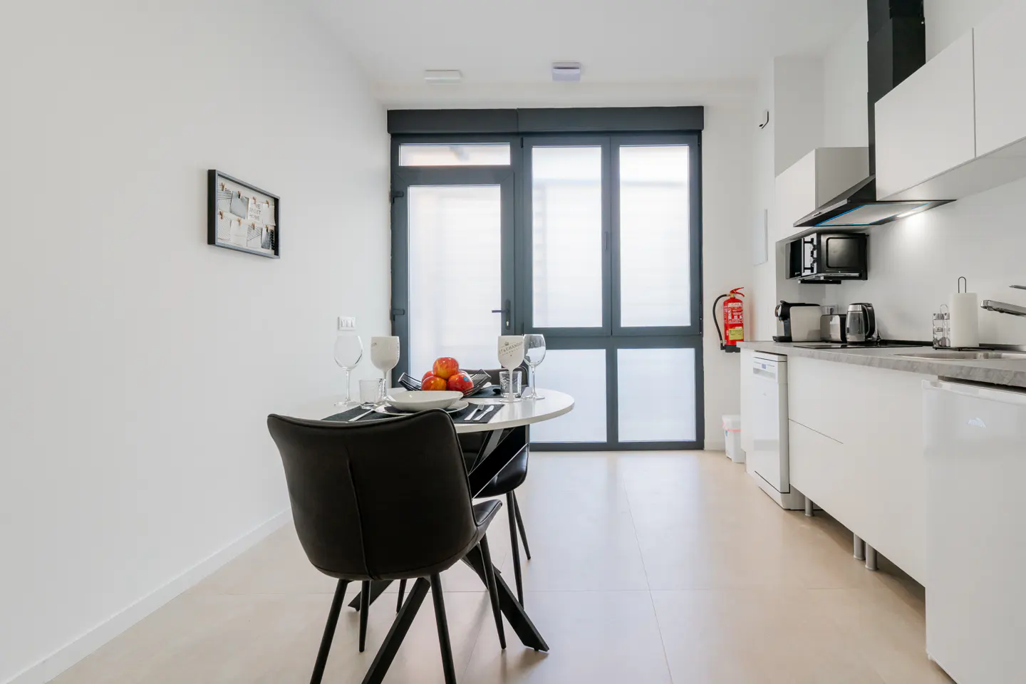 Modern kitchen with white cabinets, a small round dining table with two black chairs, and a large glass door to the patio.