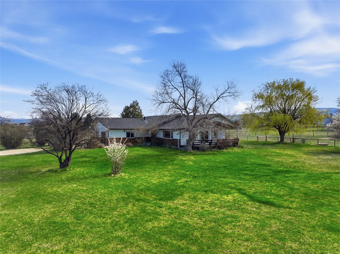 A ranch-style house with a green lawn and trees under a blue sky.