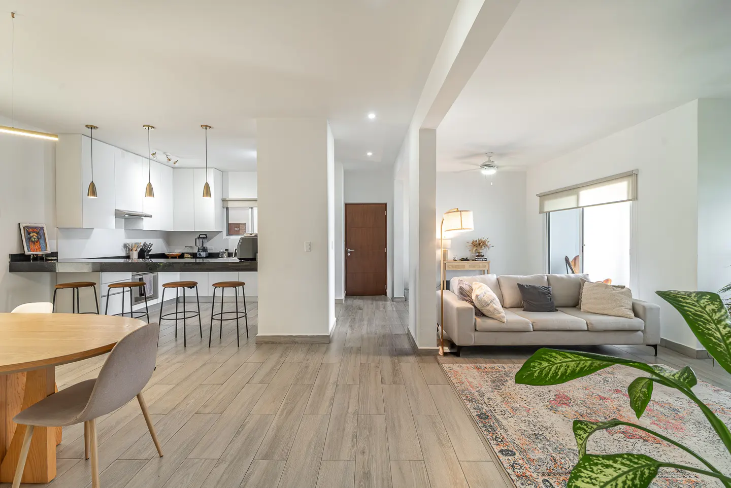 Open-concept living space with a kitchen, dining area, and living room. White walls, wood floors, and modern furniture.