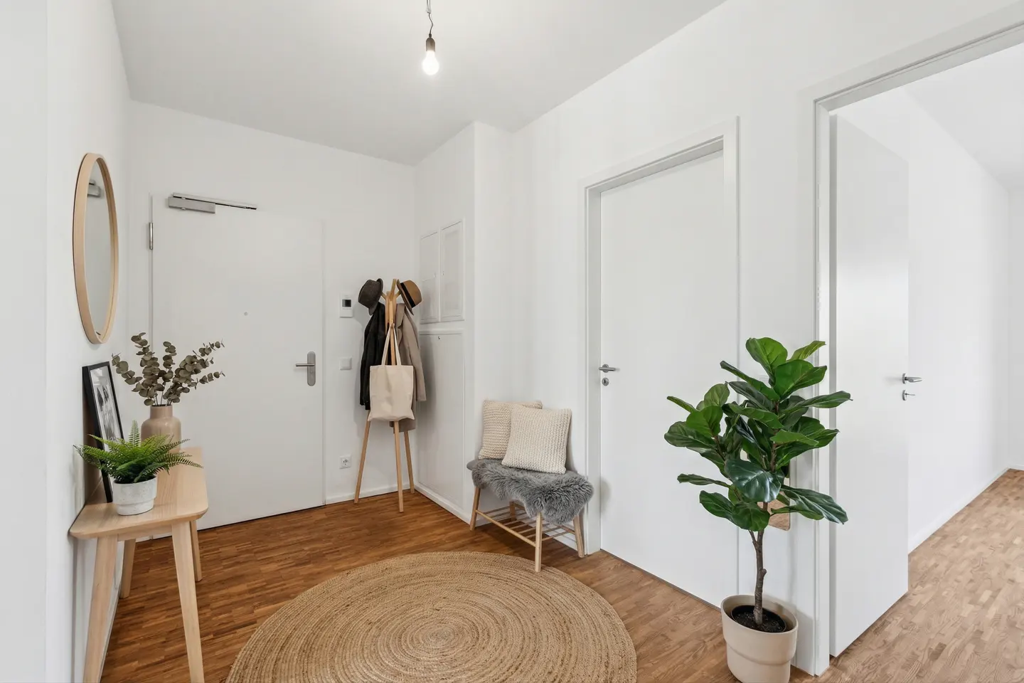 Bright entryway with white walls, wood floors, and a round jute rug. A console table, coat rack, and bench add functional decor.