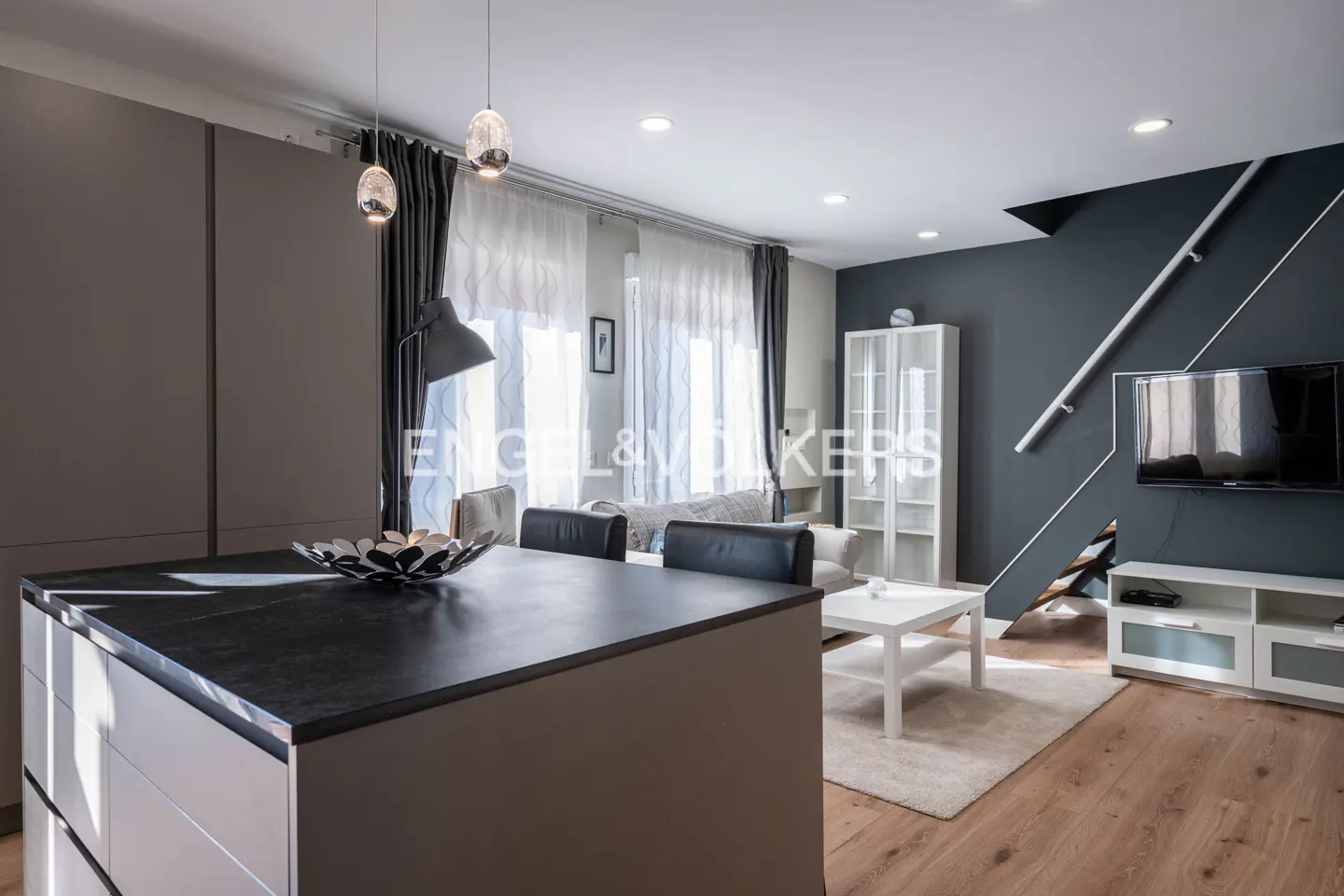 Open-concept living space with a kitchen island, gray walls, wood floors, and modern furniture. A TV is mounted on the wall.