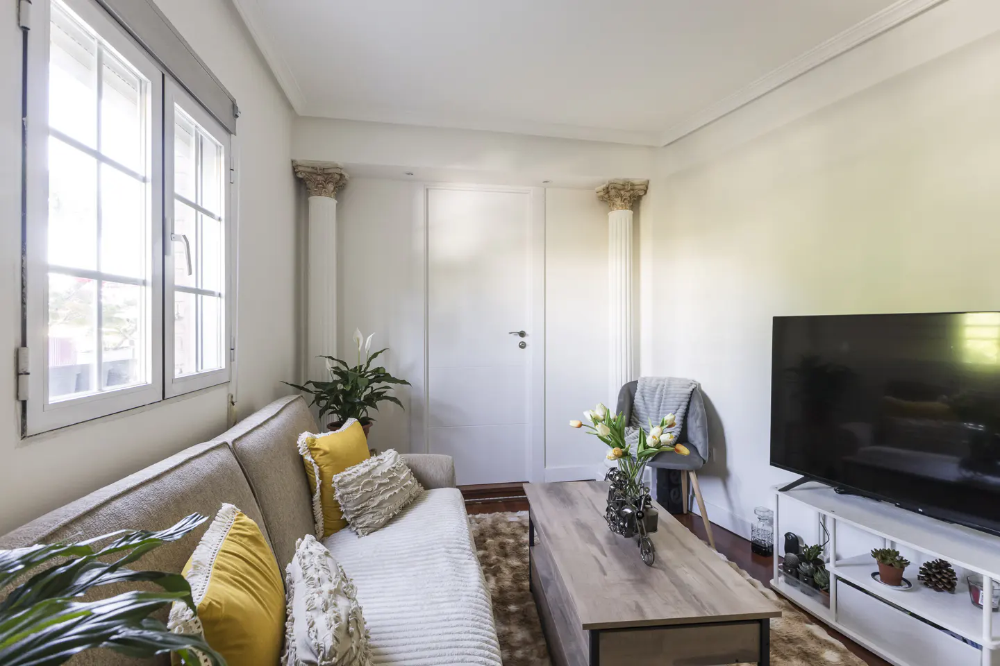 Living room with a beige sofa, yellow pillows, a wooden coffee table, and a TV on a white stand.