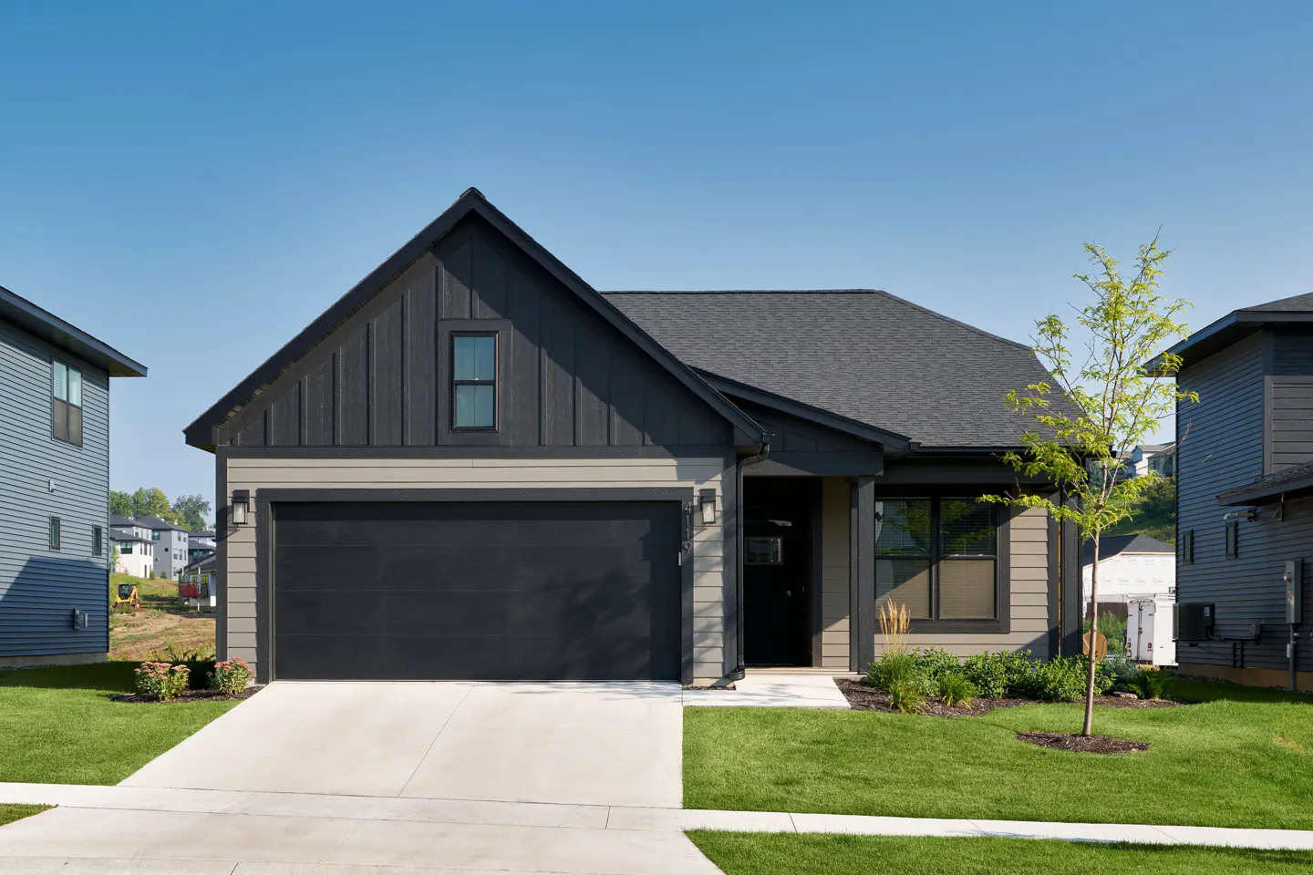A modern single-story home with a dark gray garage door, gray siding, and a well-manicured lawn under a clear blue sky.
