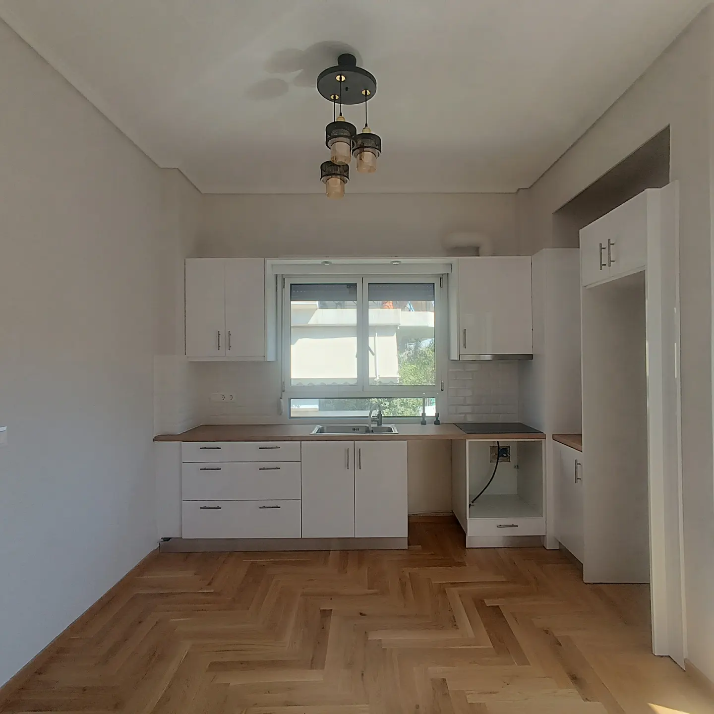 Bright kitchen with white cabinets, wood countertops, and herringbone wood floor. A modern light fixture hangs from the ceiling.