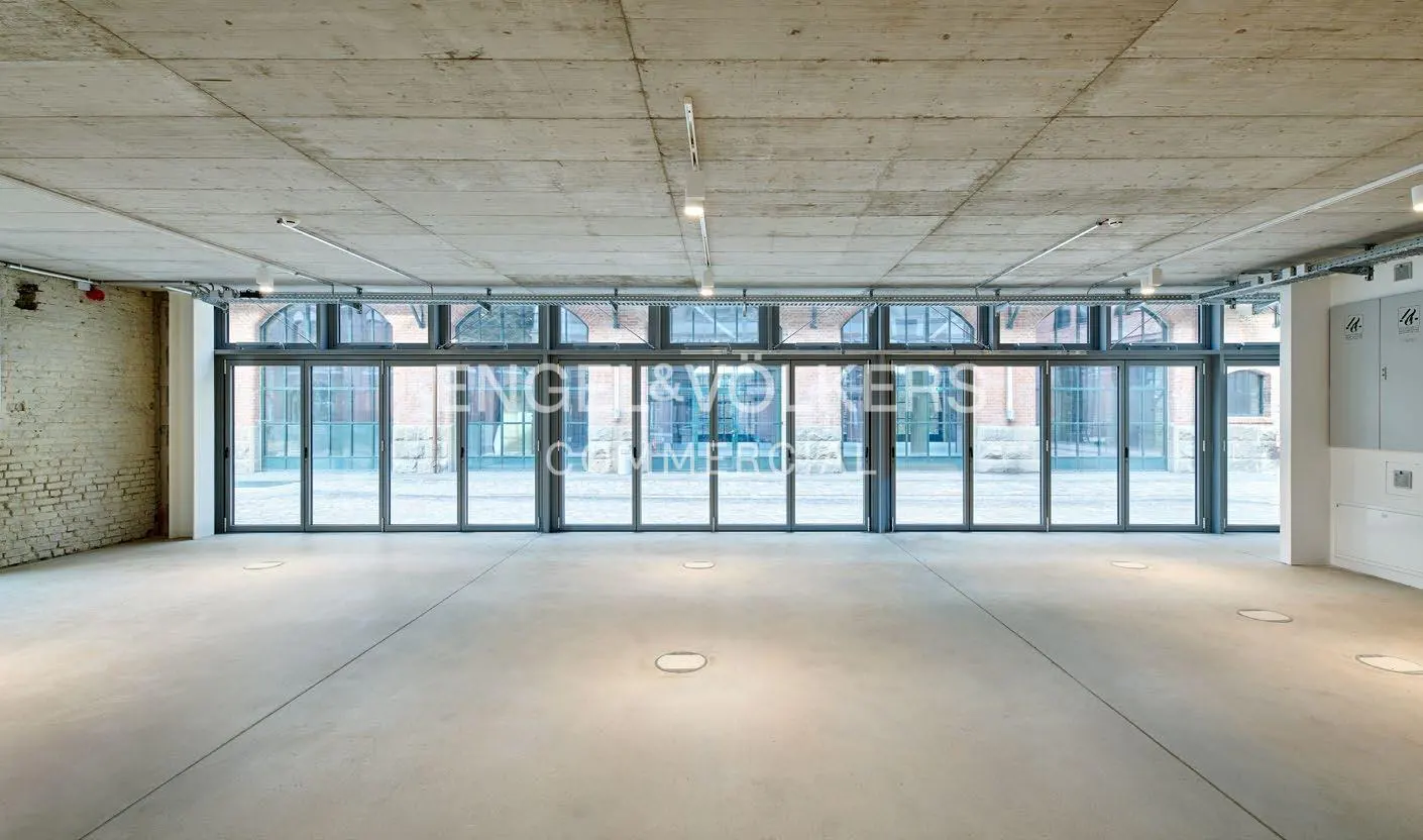 Empty commercial space with concrete floors and ceiling, and a wall of glass doors.