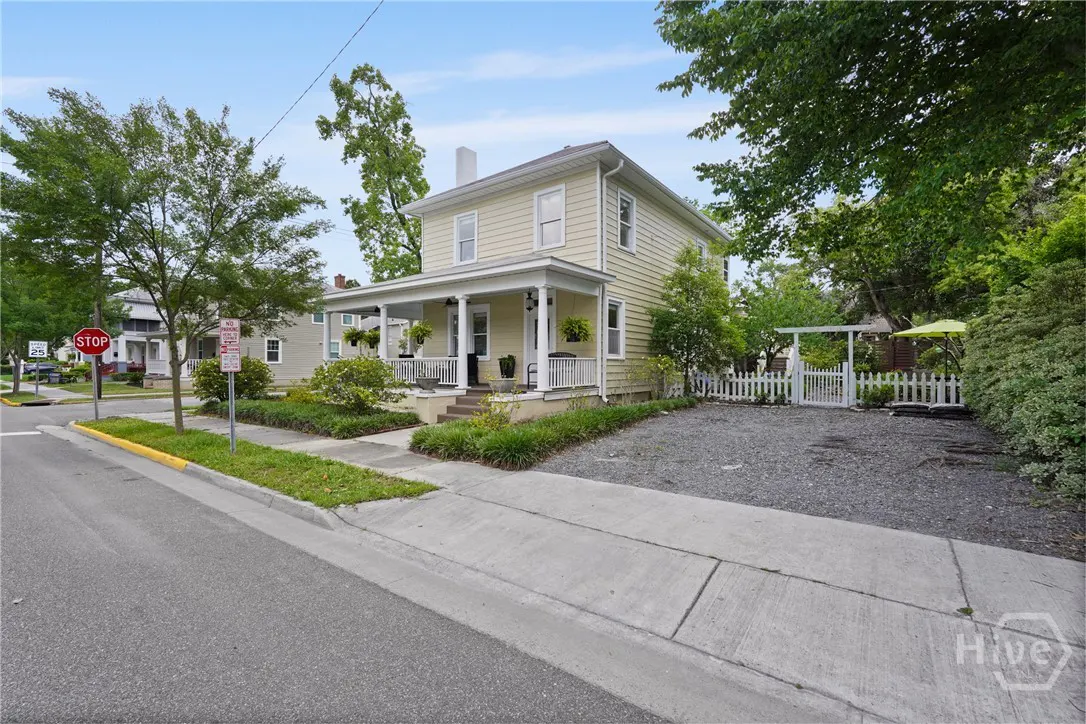 Two-story yellow house with a white porch and white picket fence on a sunny day.