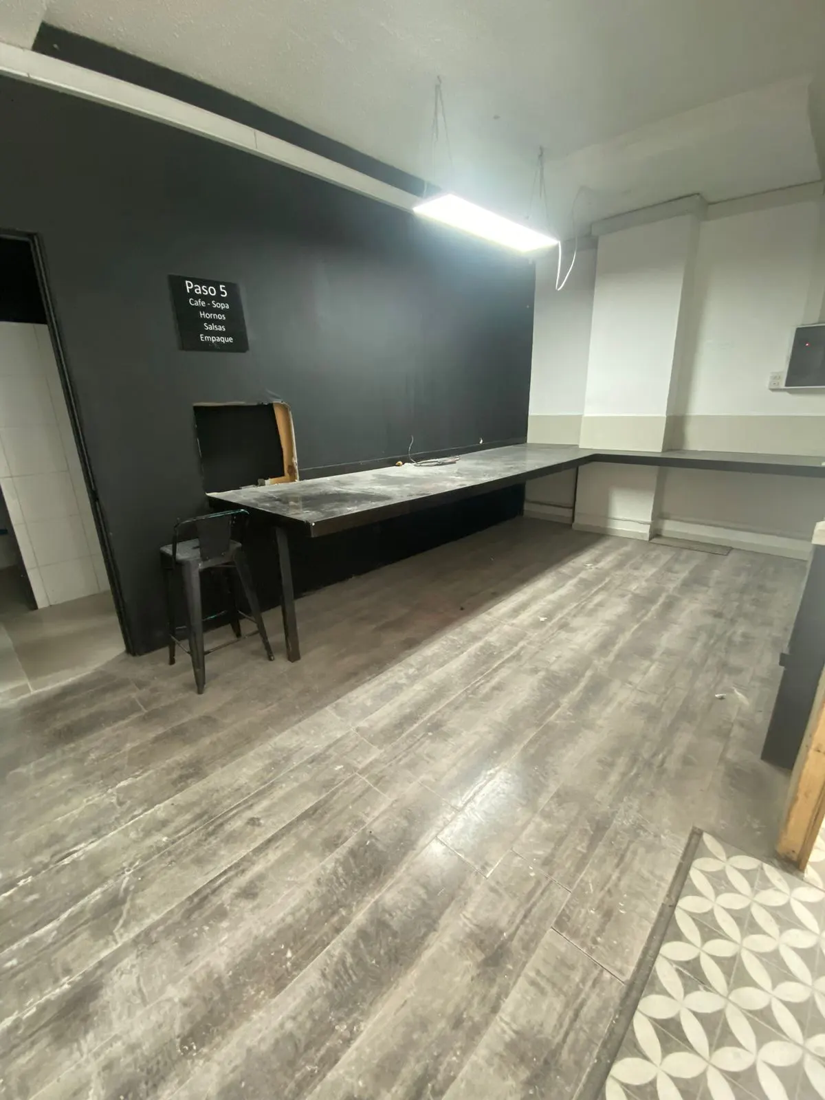 A commercial space with a long black table, a black chair, and a black wall with white text. The floor is gray wood-look tile.