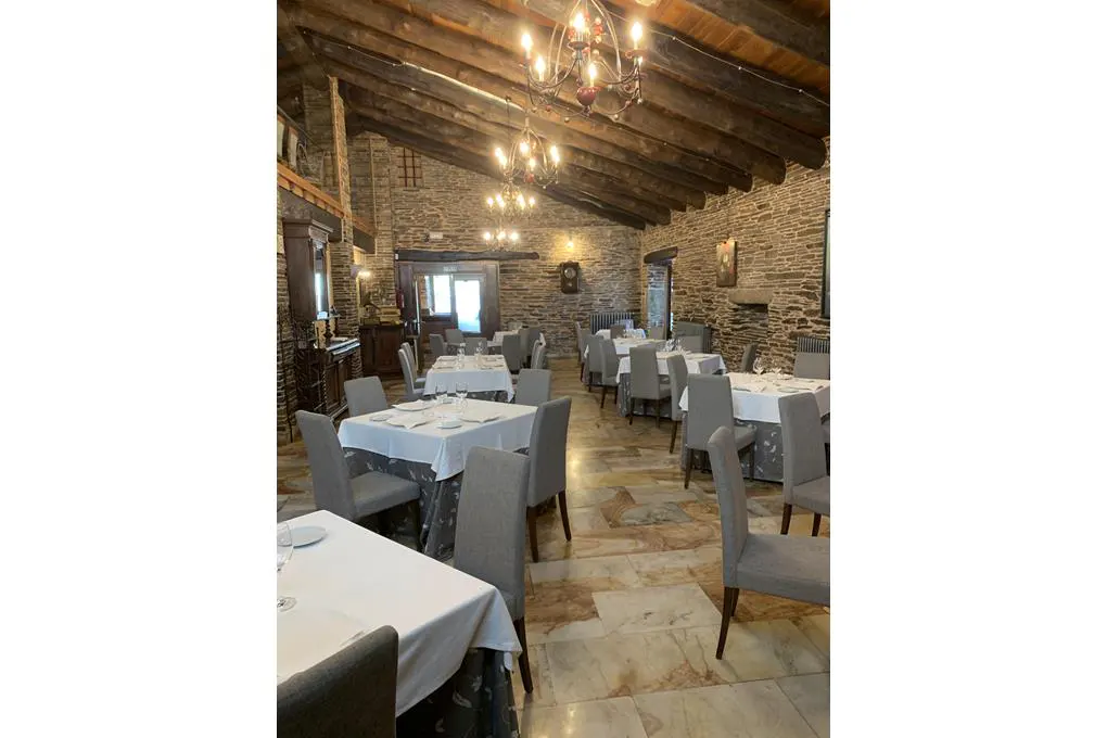Rustic restaurant interior with stone walls, exposed wooden beams, chandeliers, and tables set with white tablecloths.