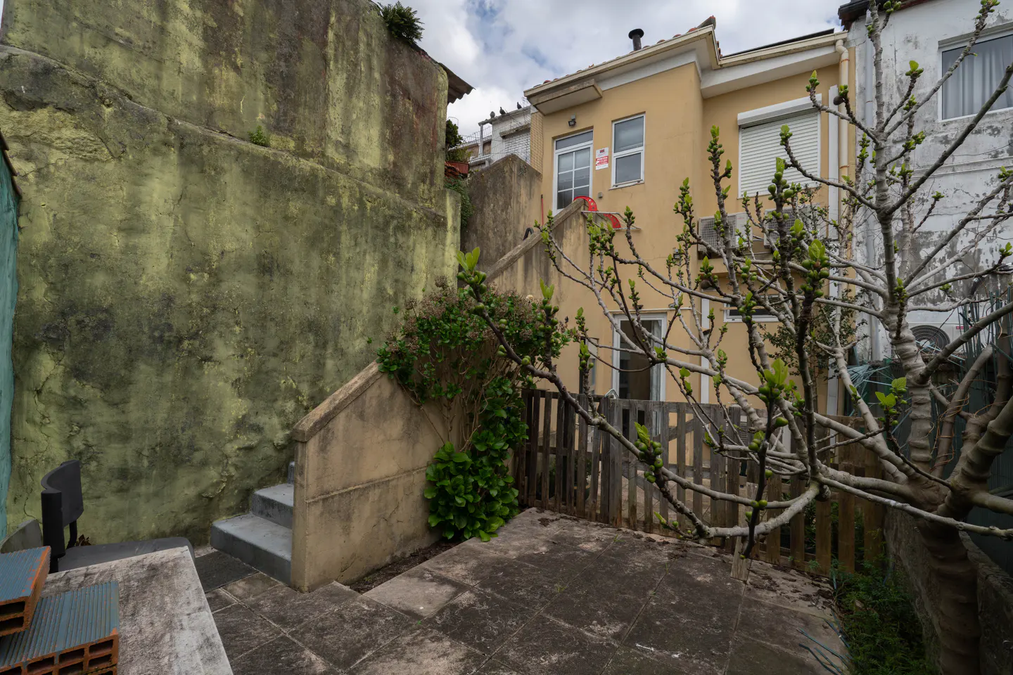 Exterior view of a yellow two-story house with a small backyard and a concrete staircase leading up to the house.