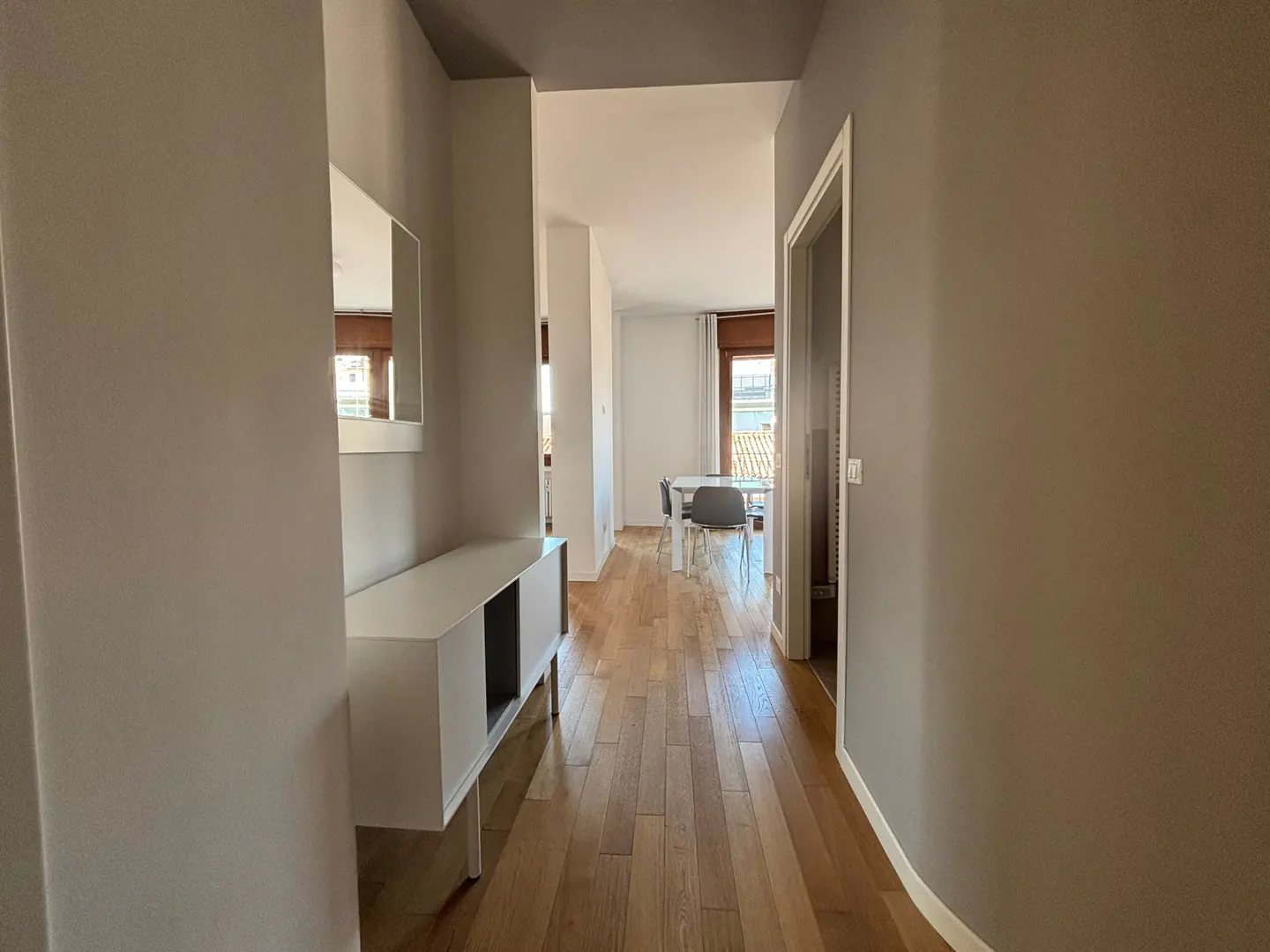 Hallway with wood floors, gray walls, and a white console table with a mirror above it. A dining table is visible in the background.