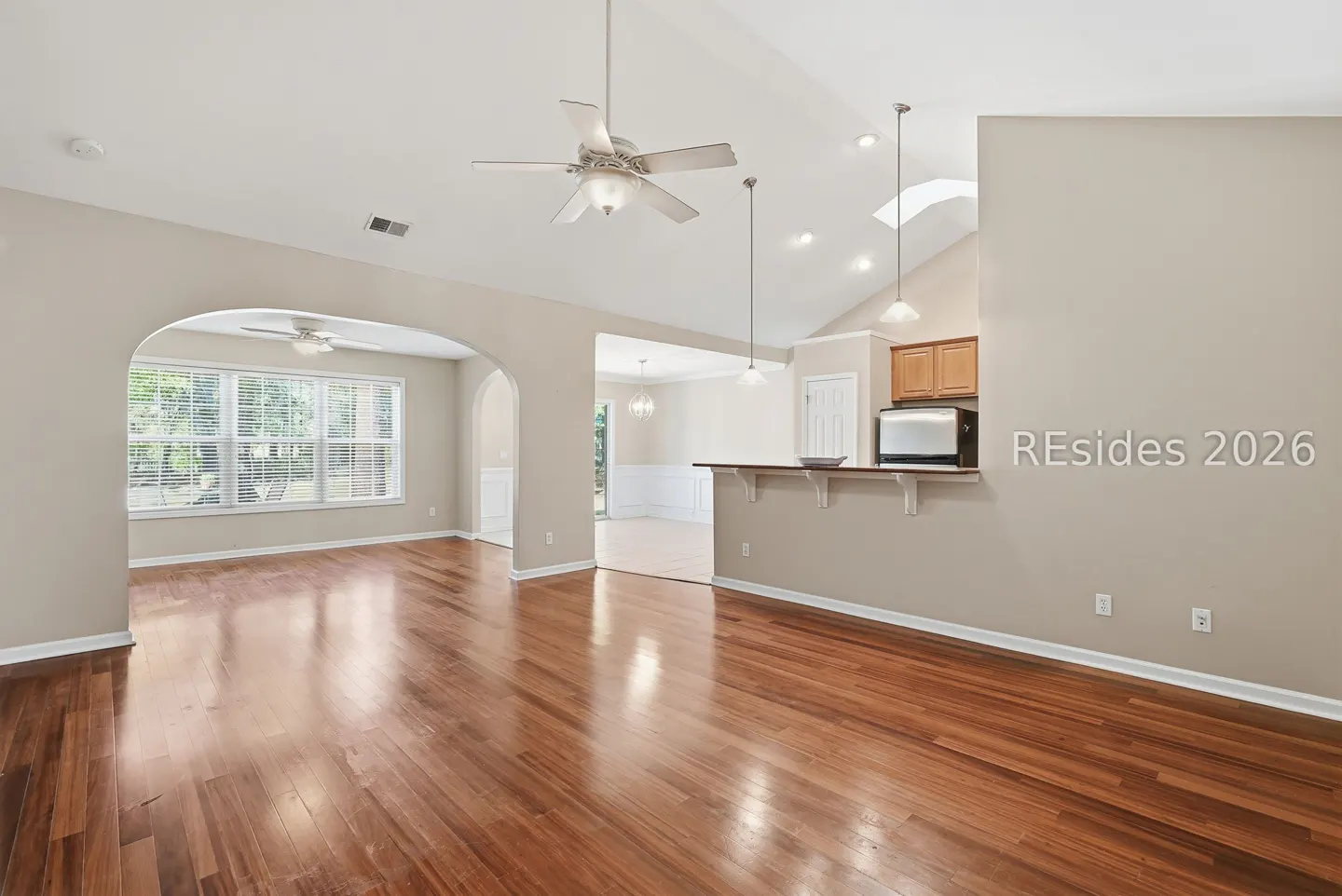 Open-concept home interior with hardwood floors, beige walls, ceiling fans, and arched doorways.