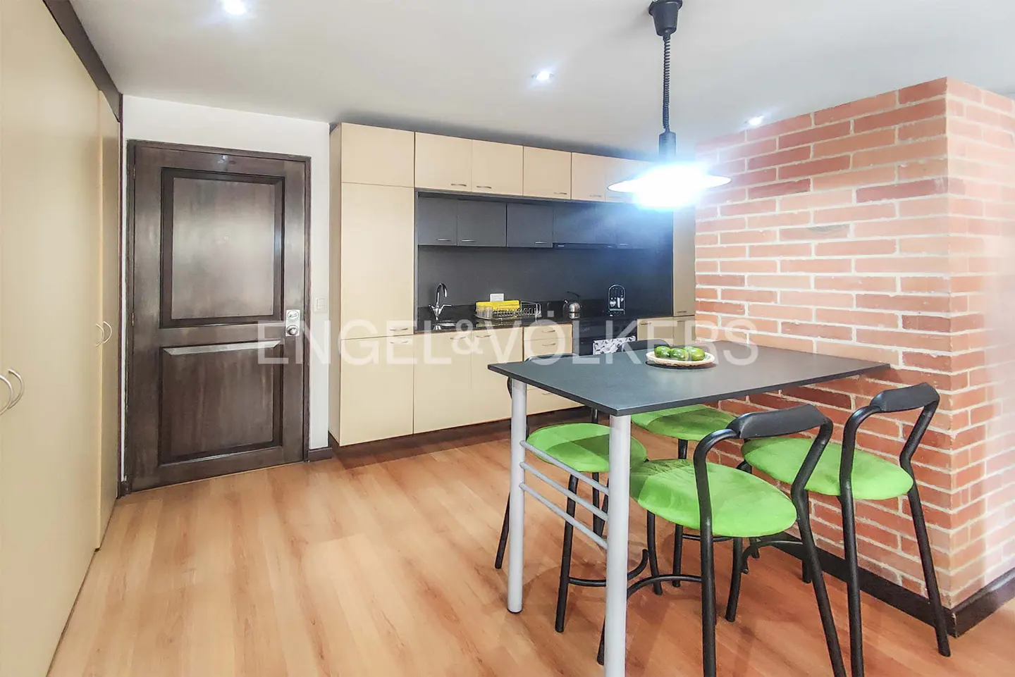 A modern kitchen with a black table, green chairs, and brick wall.
