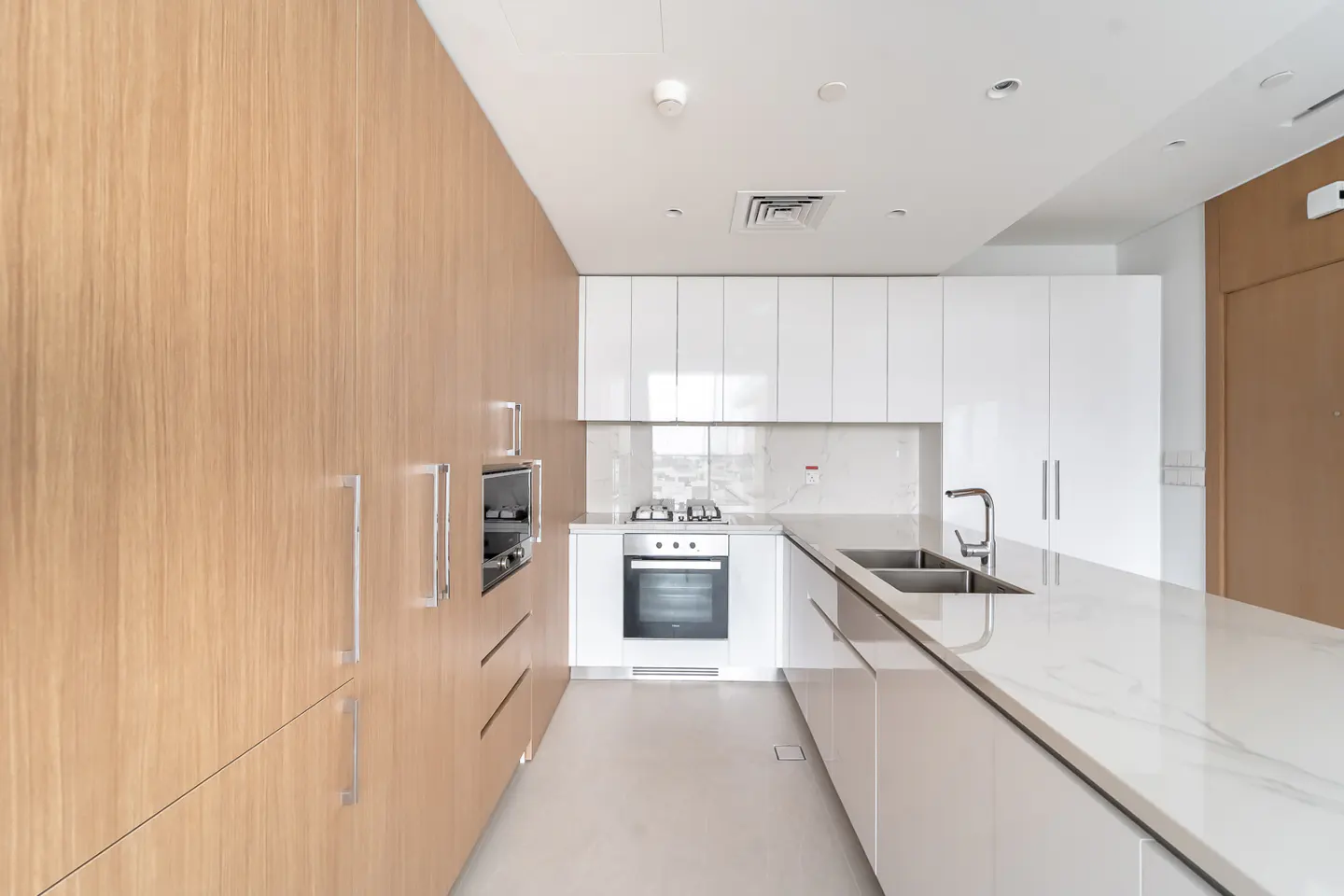 A modern kitchen with light wood cabinets, white upper cabinets, and a marble countertop island. Stainless steel appliances are visible.