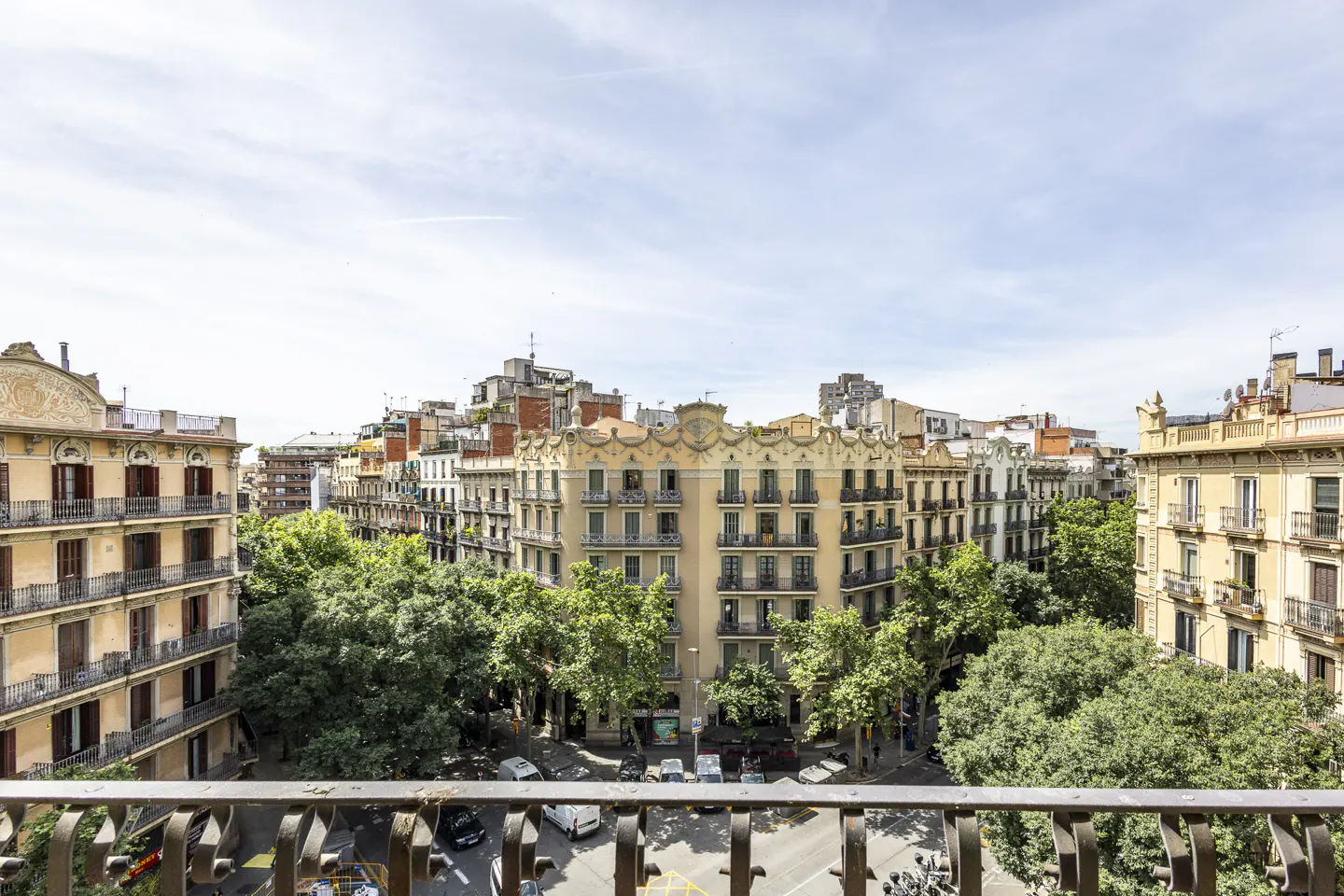 View from a balcony overlooking a tree-lined street with historic yellow apartment buildings under a bright blue sky.