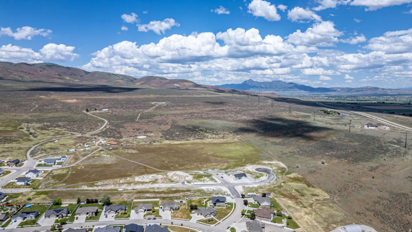 Aerial view of a suburban neighborhood bordering a vast, dry landscape with rolling hills and mountains under a blue sky.