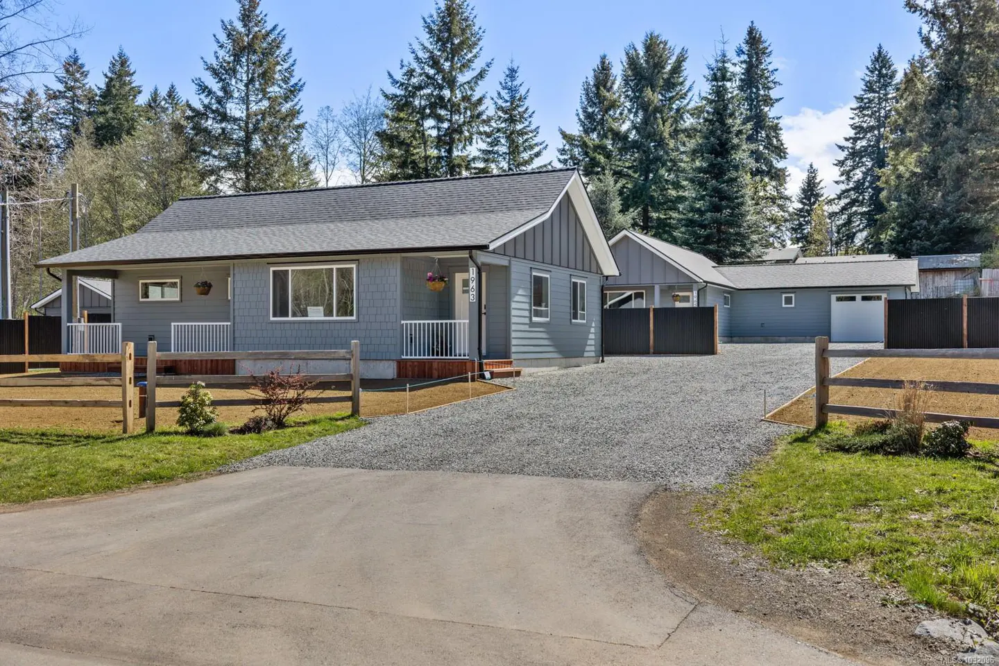 Exterior of a gray house with a gray roof, white trim, and a gravel driveway. Trees are in the background.