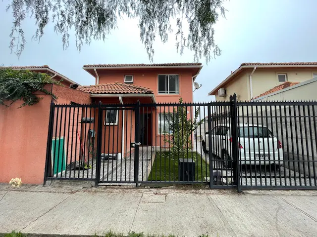 Two-story peach house with a red tile roof, viewed through a black iron fence. A white car is parked in the driveway.
