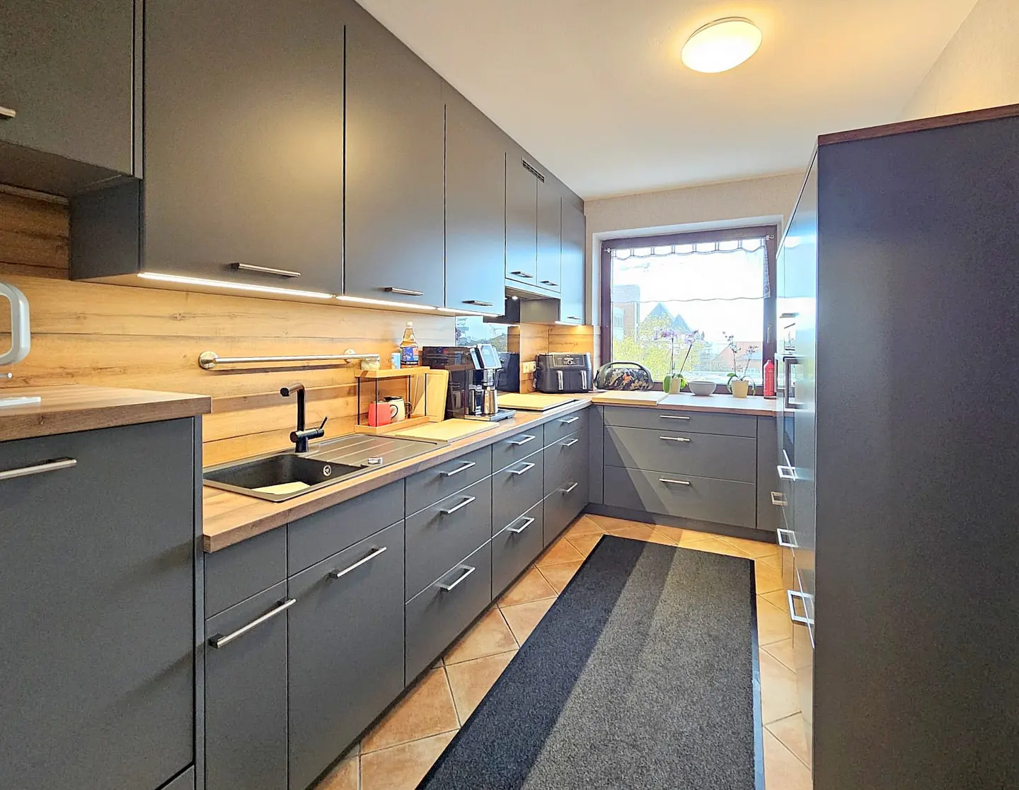 Modern kitchen with gray cabinets, wood countertops, and a black sink. A window provides natural light.