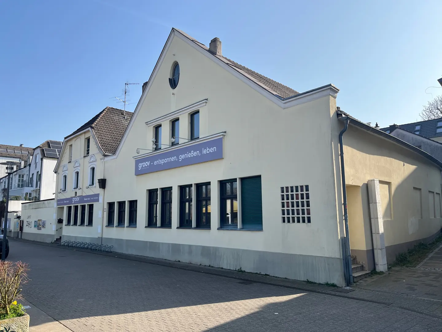 A cream-colored commercial building with a purple sign reading "groov - entspannen, genießen, leben" on a sunny day.