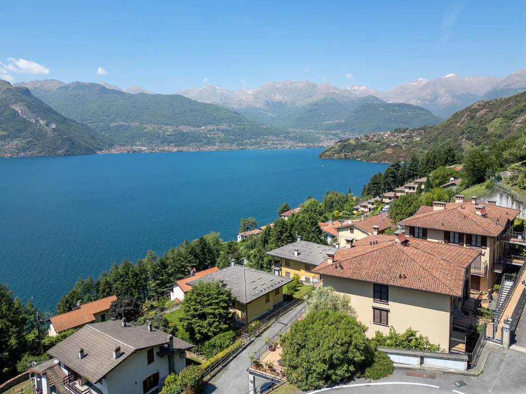 High-angle view of houses with terracotta roofs overlooking a deep blue lake surrounded by mountains under a clear sky.
