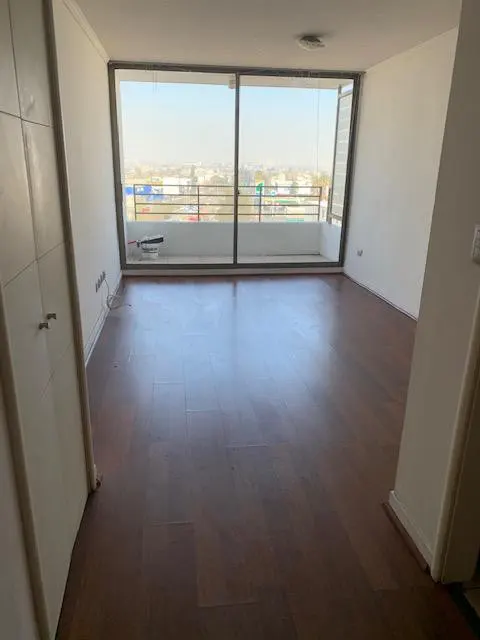 Empty room with dark wood floors, white walls, and a large window with a city view. A white closet is on the left.