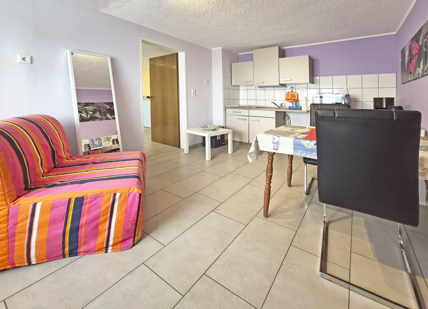A bright apartment interior with a striped sofa, kitchen, and dining area.