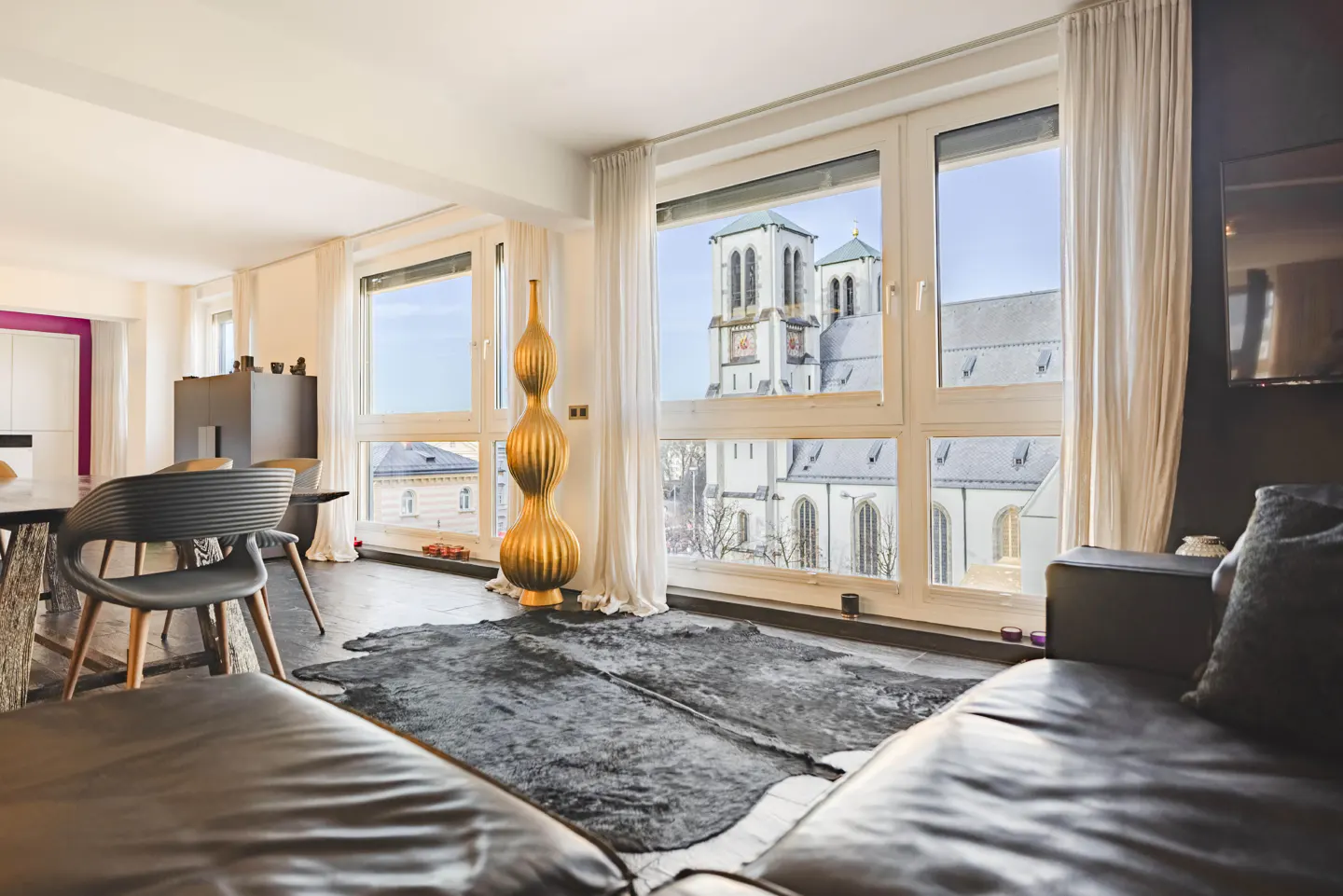 A modern living room with a leather sofa, a cowhide rug, and a view of a church through large windows.