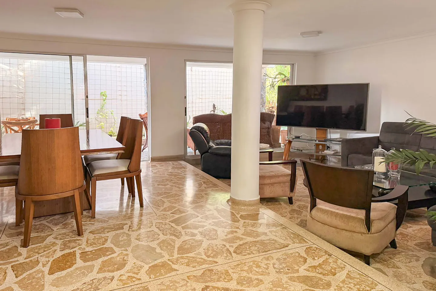 Open-concept living and dining area with stone floors, a dining table with wooden chairs, and a living room with a TV and sofas.