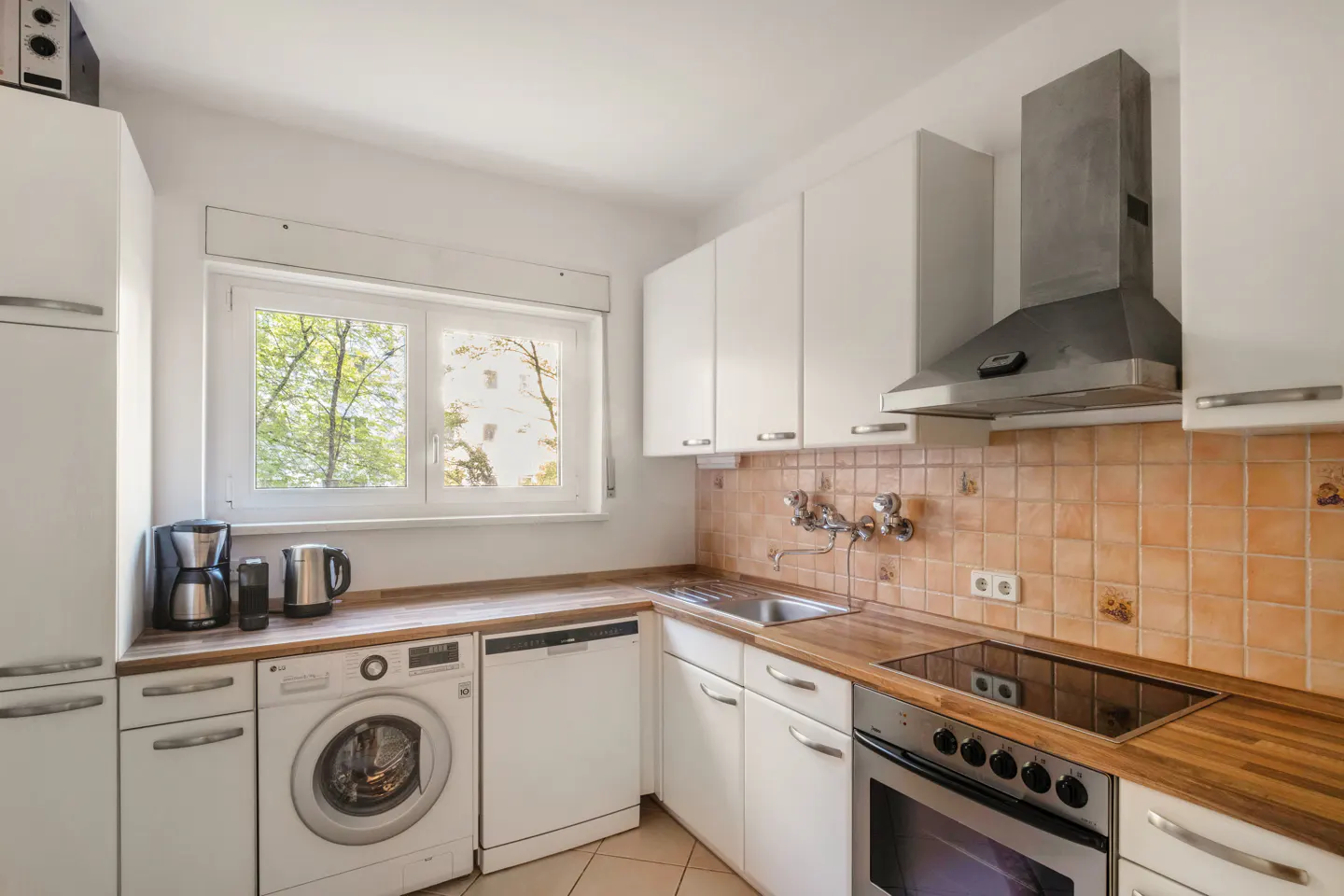 Bright kitchen with white cabinets, wood countertops, and stainless steel appliances. A window overlooks trees.