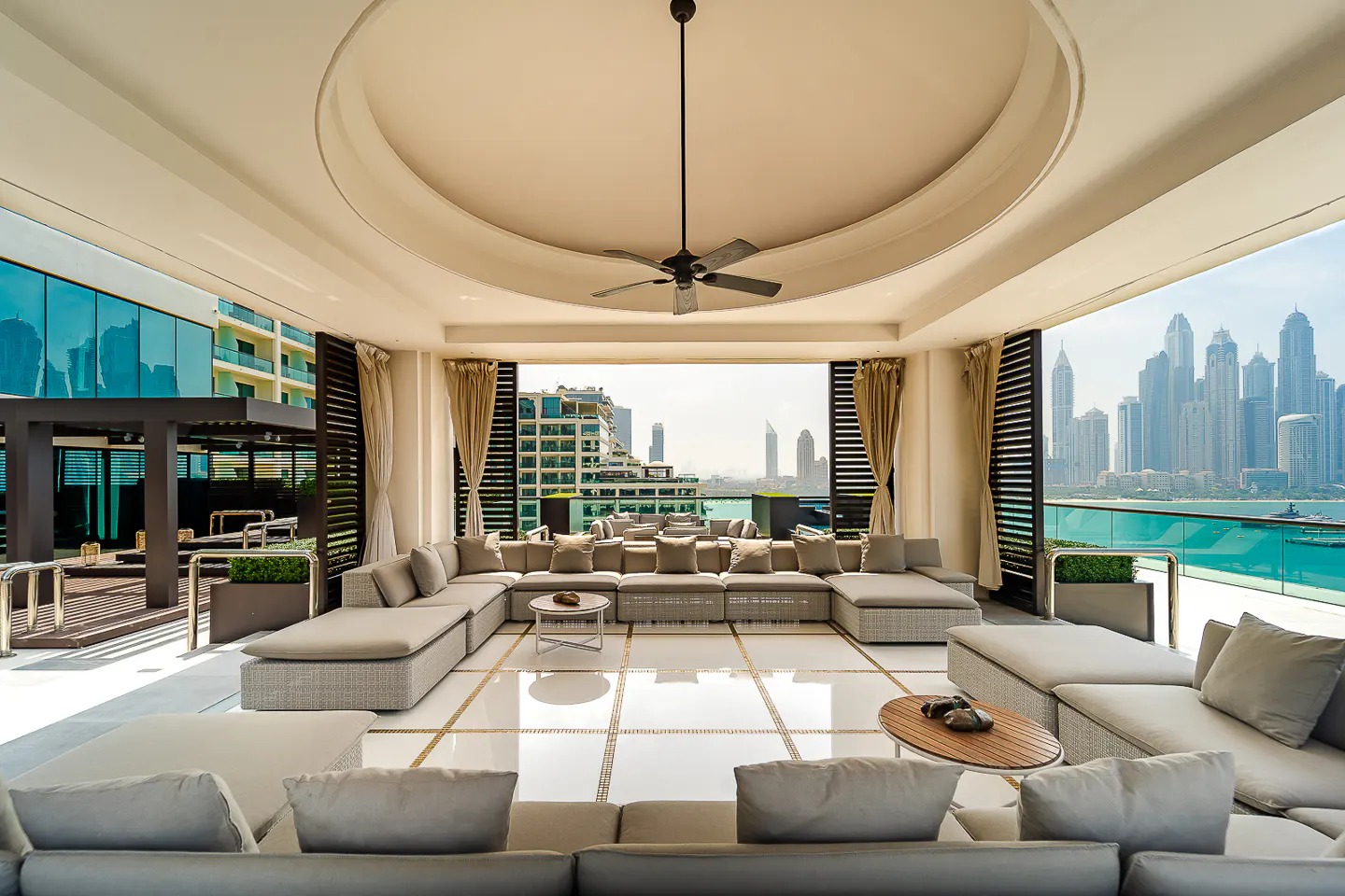 Luxury outdoor lounge with gray sectional seating, white tile floor, and a city skyline view.