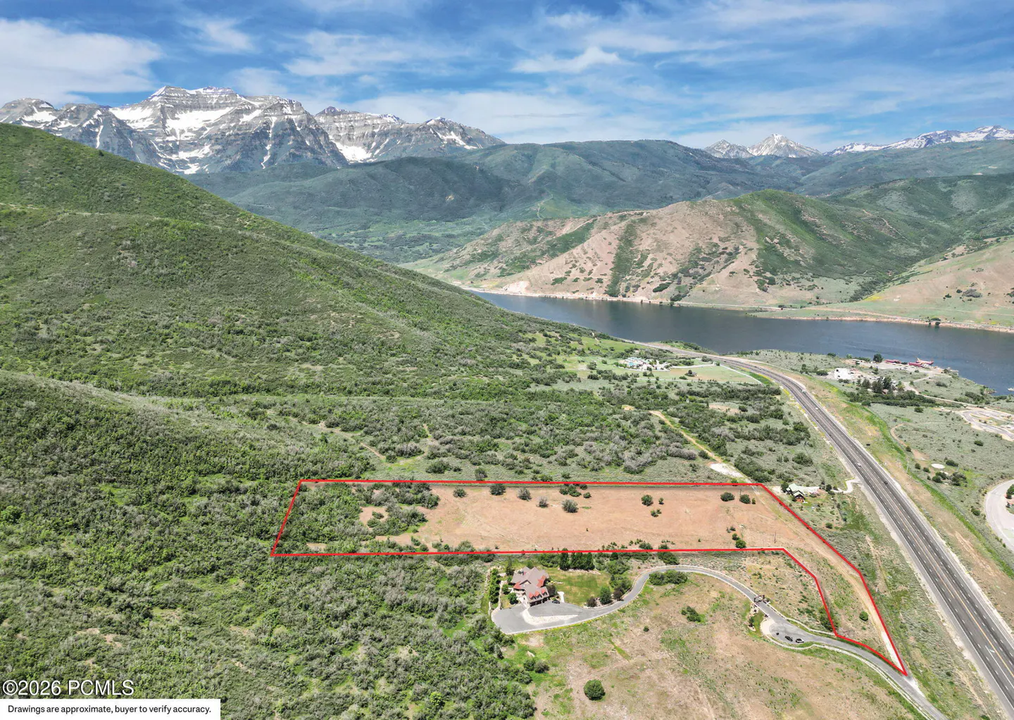 Aerial view of a property outlined in red, with mountains, a lake, and a highway in the background.