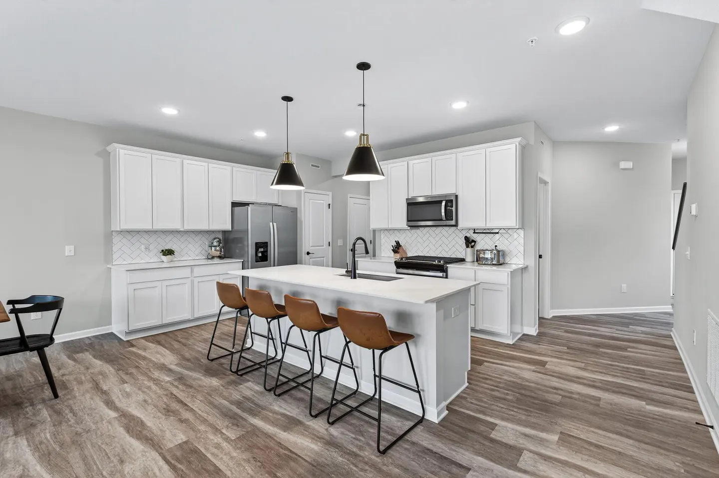 Bright kitchen with white cabinets, stainless steel appliances, and wood-look floors. A white island has seating for four with brown leather stools.