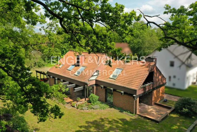 Aerial view of a brick house with a red tile roof and skylights, surrounded by green trees.