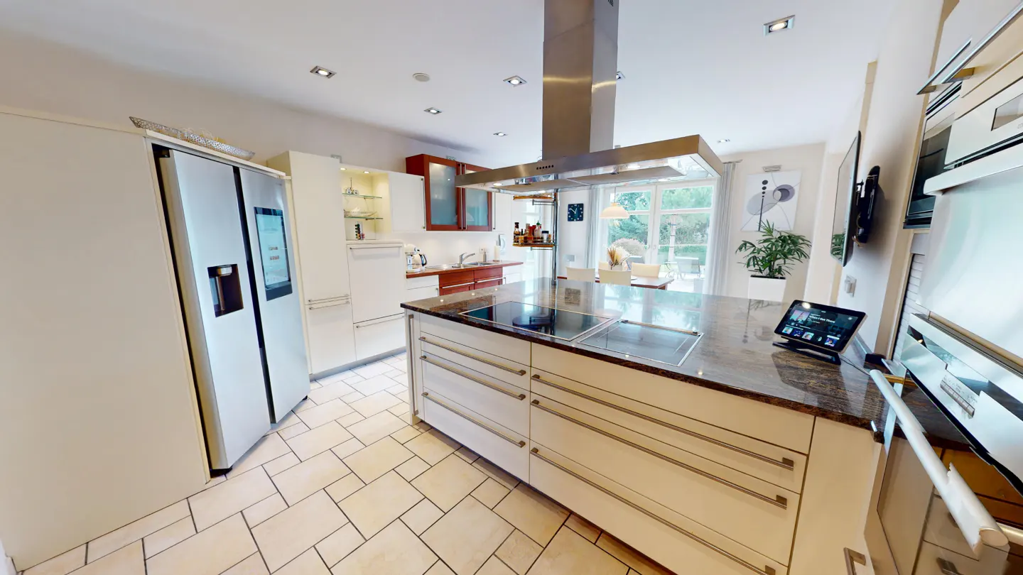 A modern kitchen with white cabinets, stainless steel appliances, and a large island with a cooktop. A tablet sits on the counter.