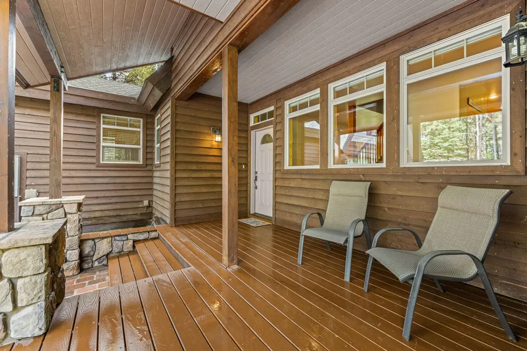 Covered porch with two chairs on a brown wood deck. The house has brown wood siding and white trim around the windows and door.