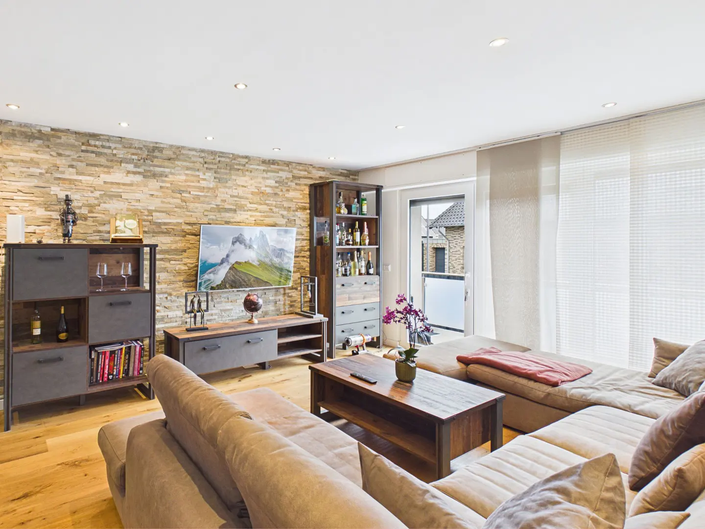 Modern living room with a stone accent wall, large sectional sofa, wooden coffee table, and a tall bar cabinet.