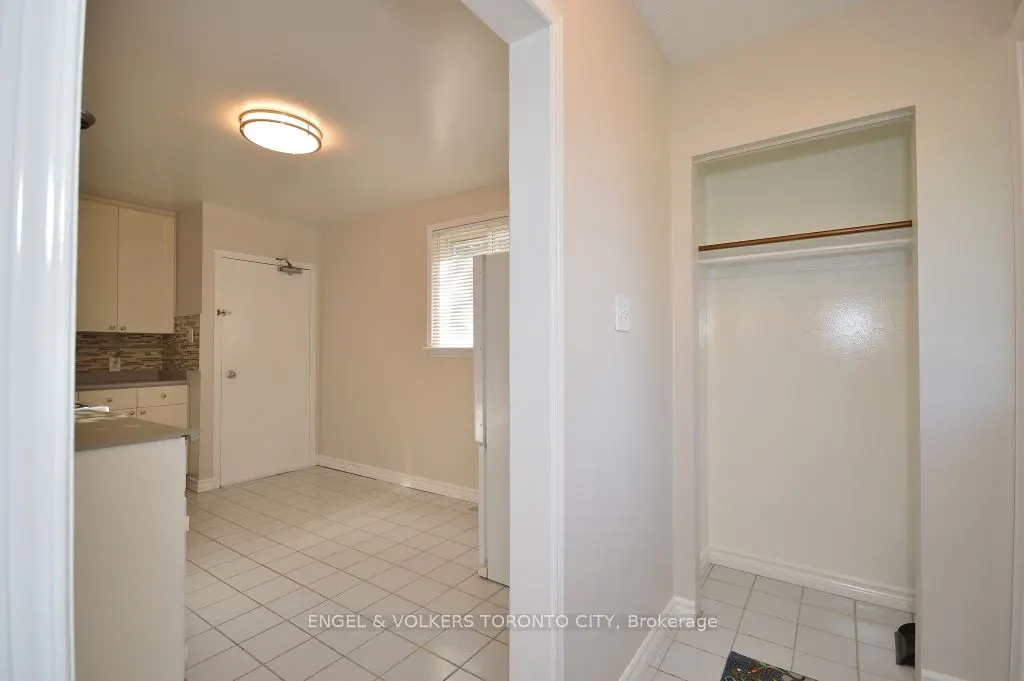 A bright, neutral-toned kitchen with white cabinets, tiled floors, and an open closet with a rod.