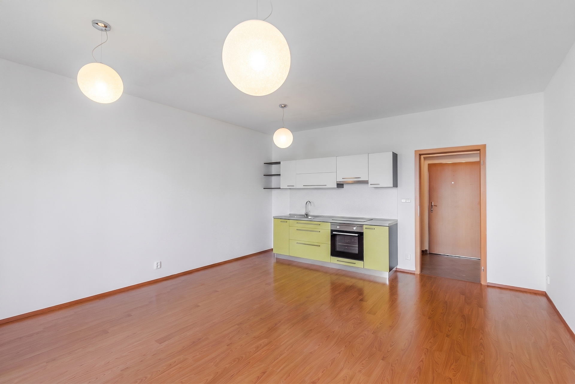Minimalist studio apartment with light green lower cabinets, white upper cabinets, wood floors, and three globe pendants.
