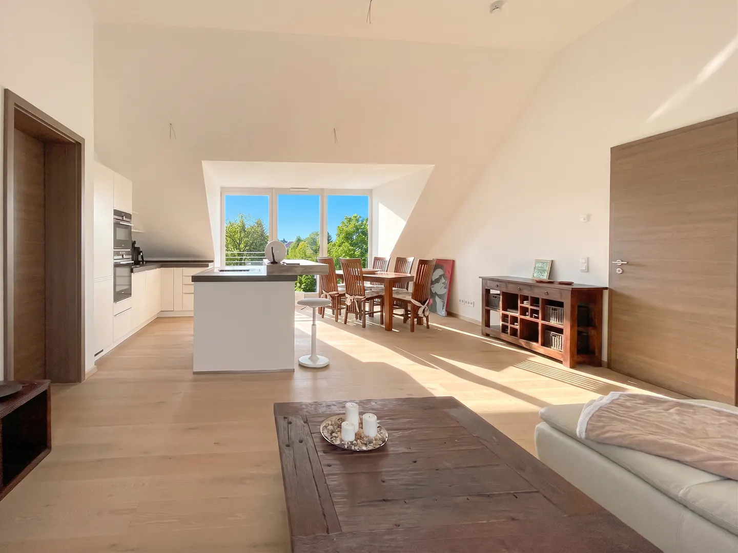 Bright open-plan attic apartment with a modern kitchen, dining area, and wooden coffee table under a sloped ceiling.