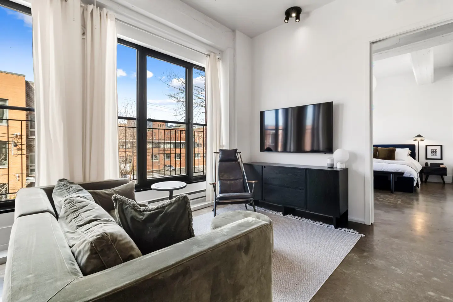 Living room with a gray couch, black TV console, and a view of a bedroom through a doorway.