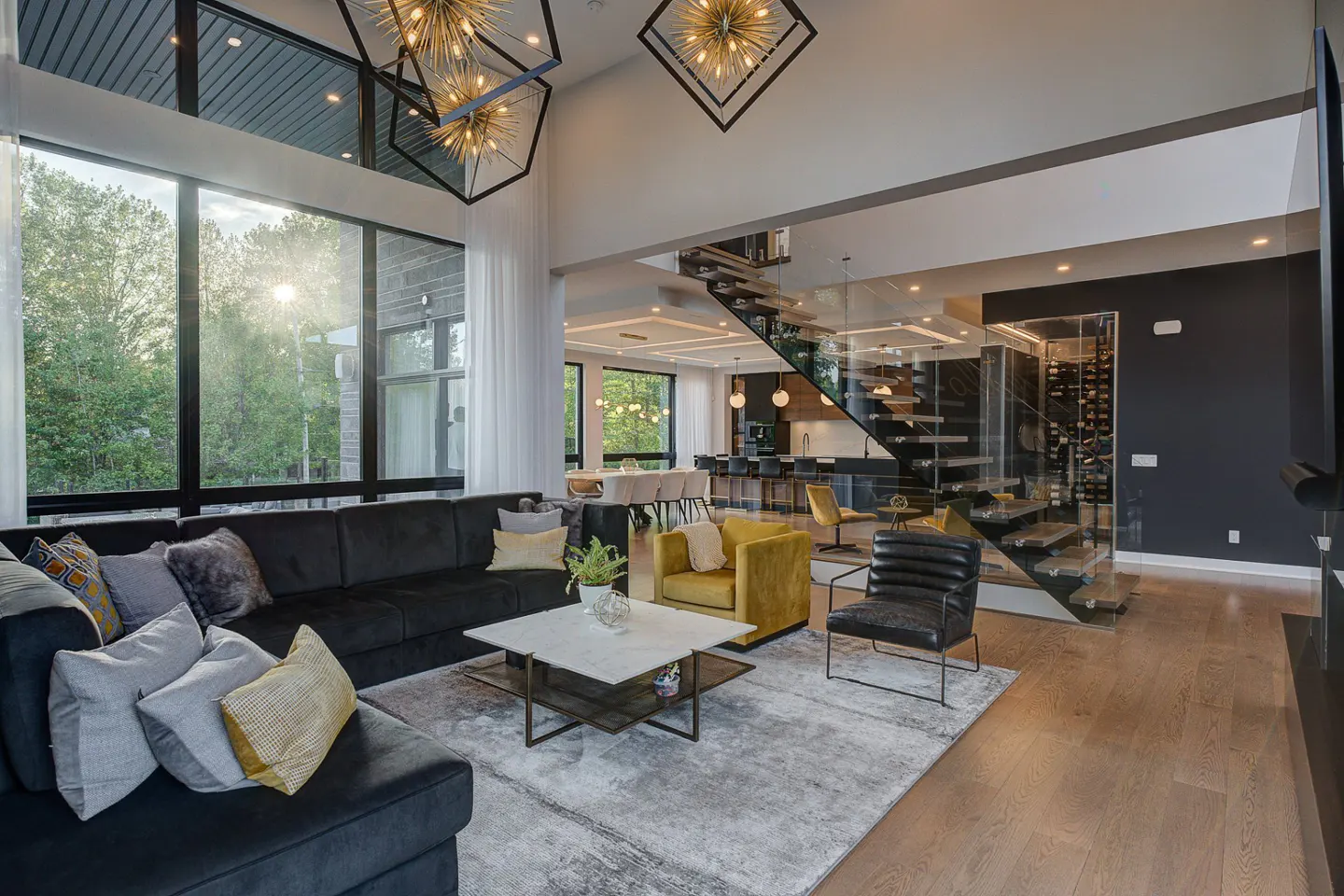A modern living room with a black sectional sofa, marble coffee table, and a glass staircase leading to a wine cellar.